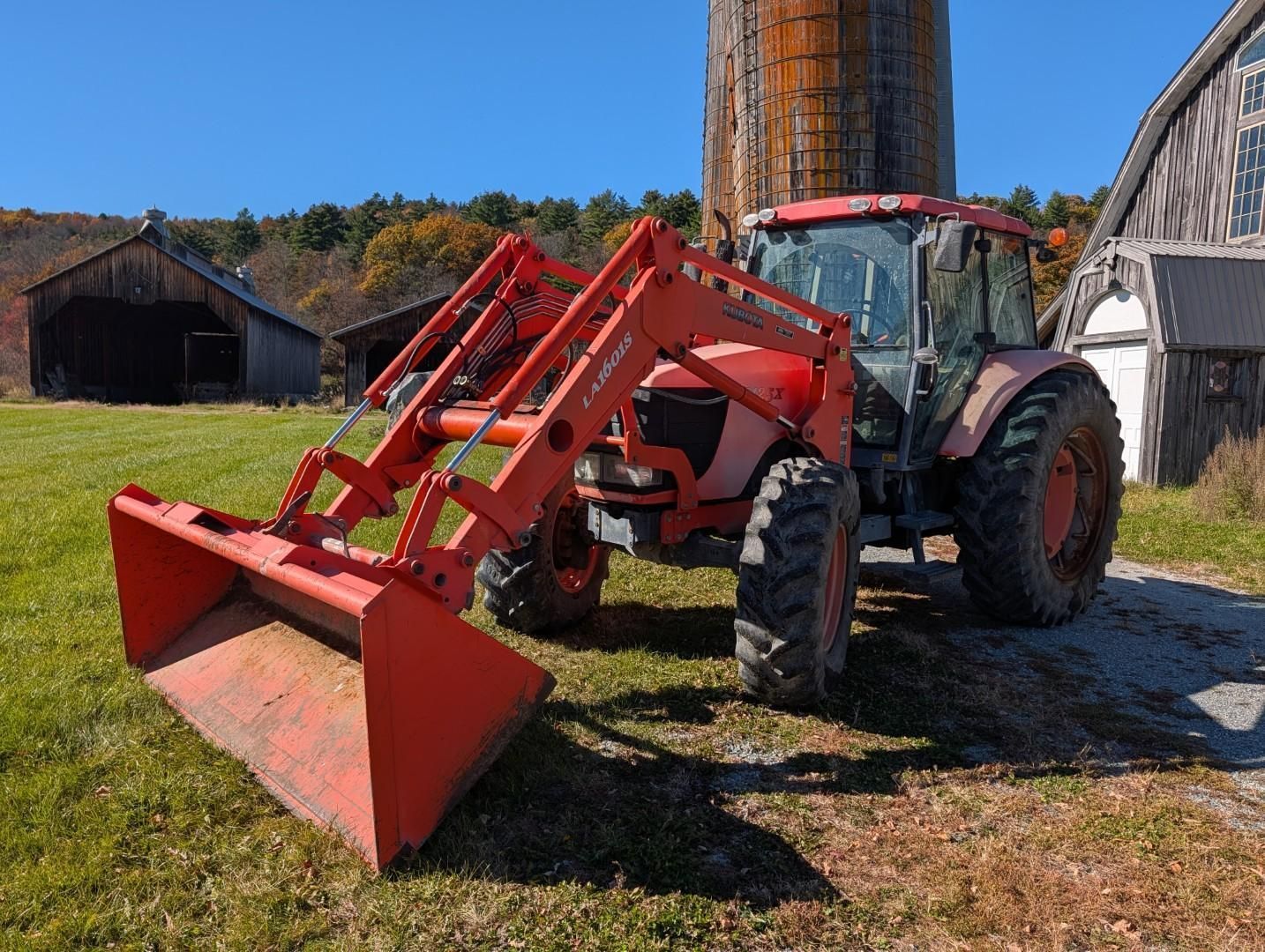Red tractor with front loader parked in a farmyard beside barns on a sunny day