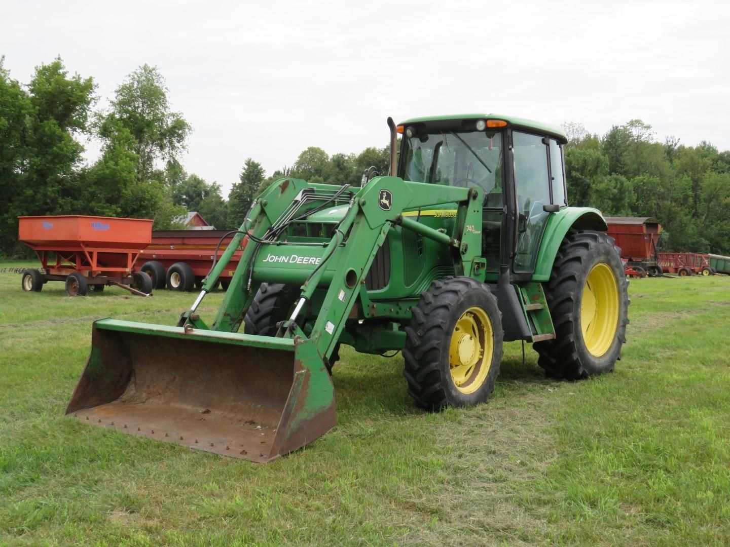 Green John Deere tractor with front loader on a grassy field.