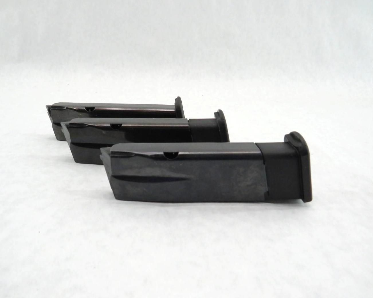 Three black pistol magazines on a white surface, angled in a row.