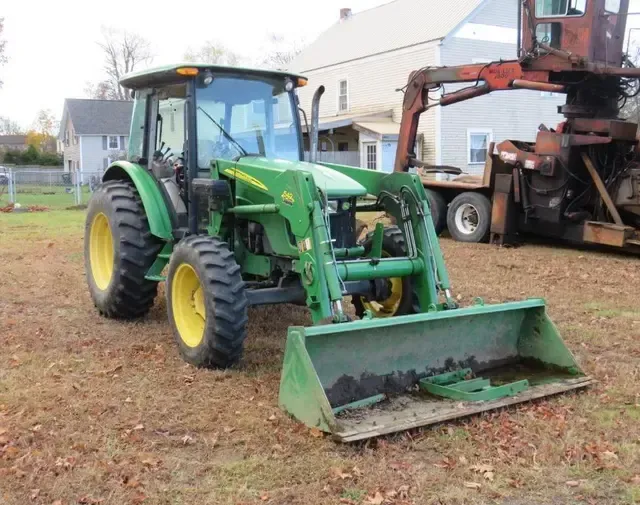 Green John Deere tractor with a front loader bucket in a grassy yard.