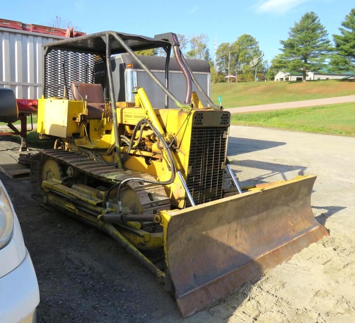 Yellow bulldozer with a blade, tracks, and canopy outdoors on a sunny day.