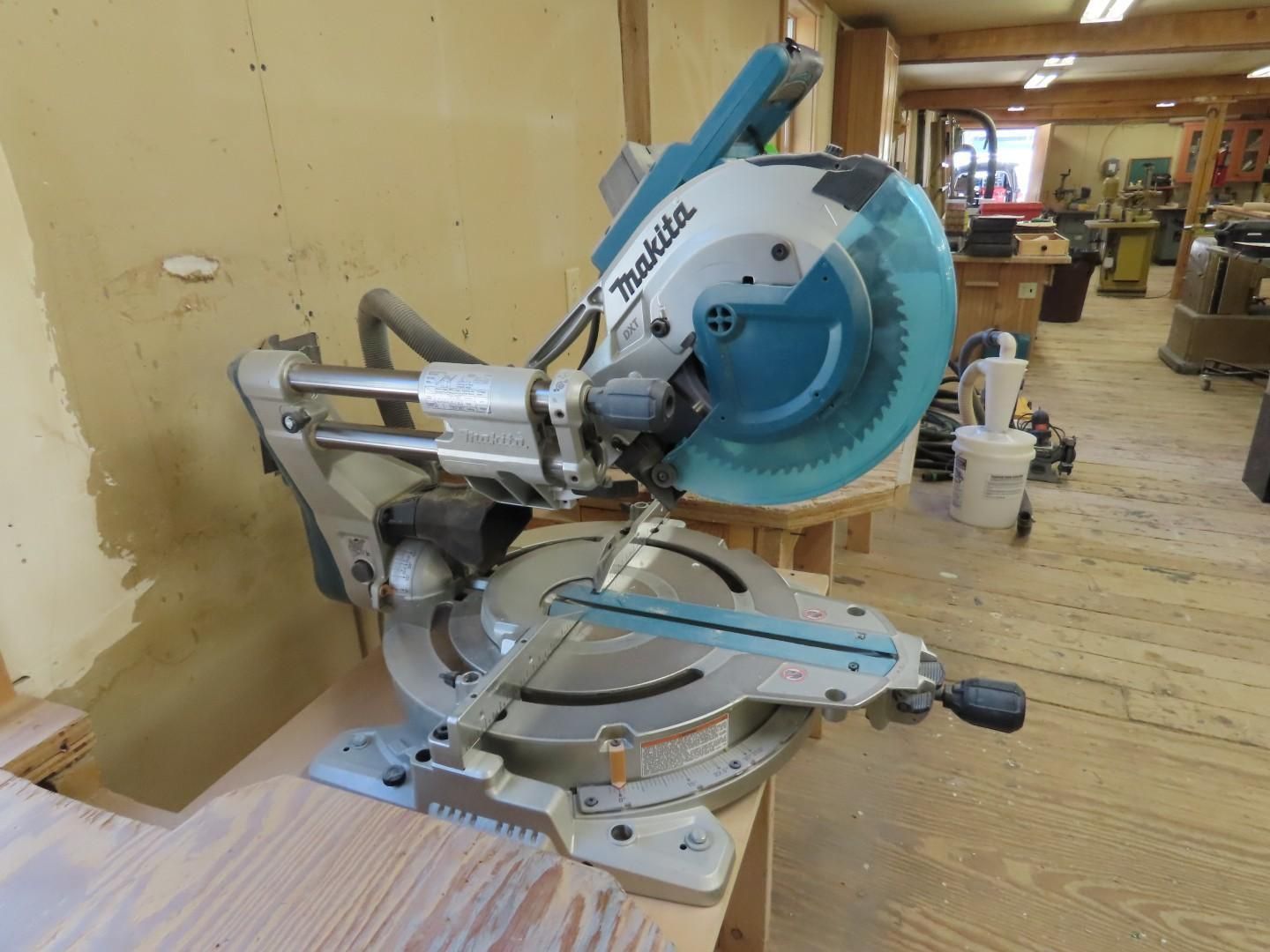 Mitre saw with blue blade on a workbench in a wood shop, viewed from the side.
