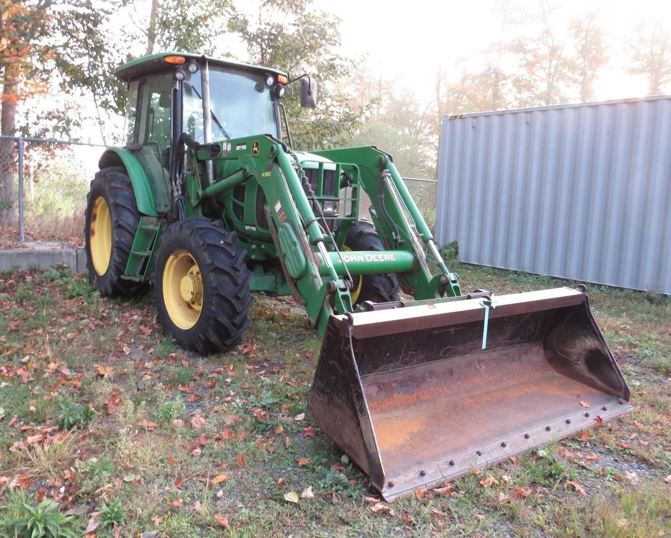 Green John Deere tractor with front loader bucket, outdoors next to a metal container.