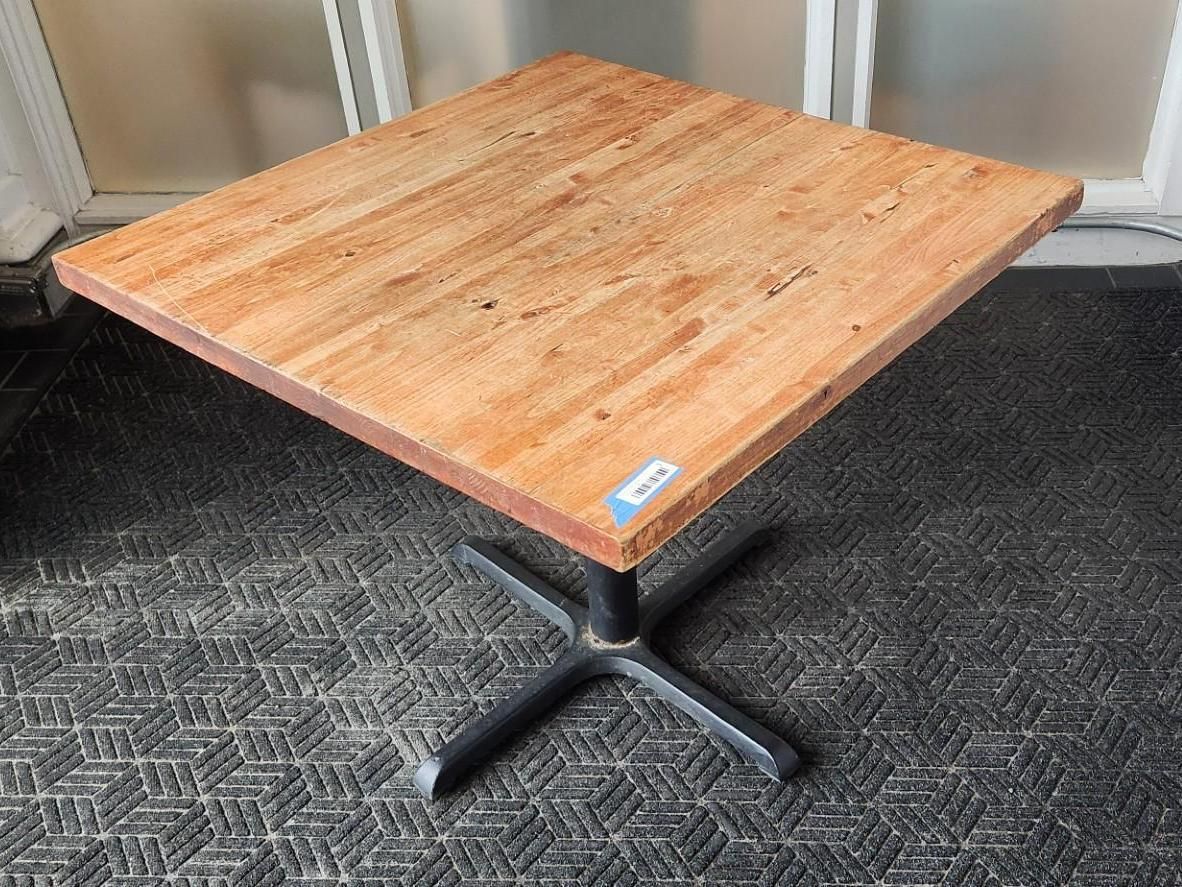 Square wooden table with a black metal base on a patterned dark gray surface.