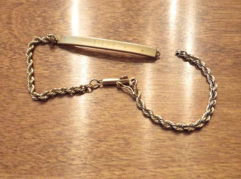 Broken gold-colored metal bracelet with a rope chain, lying on a wooden surface.