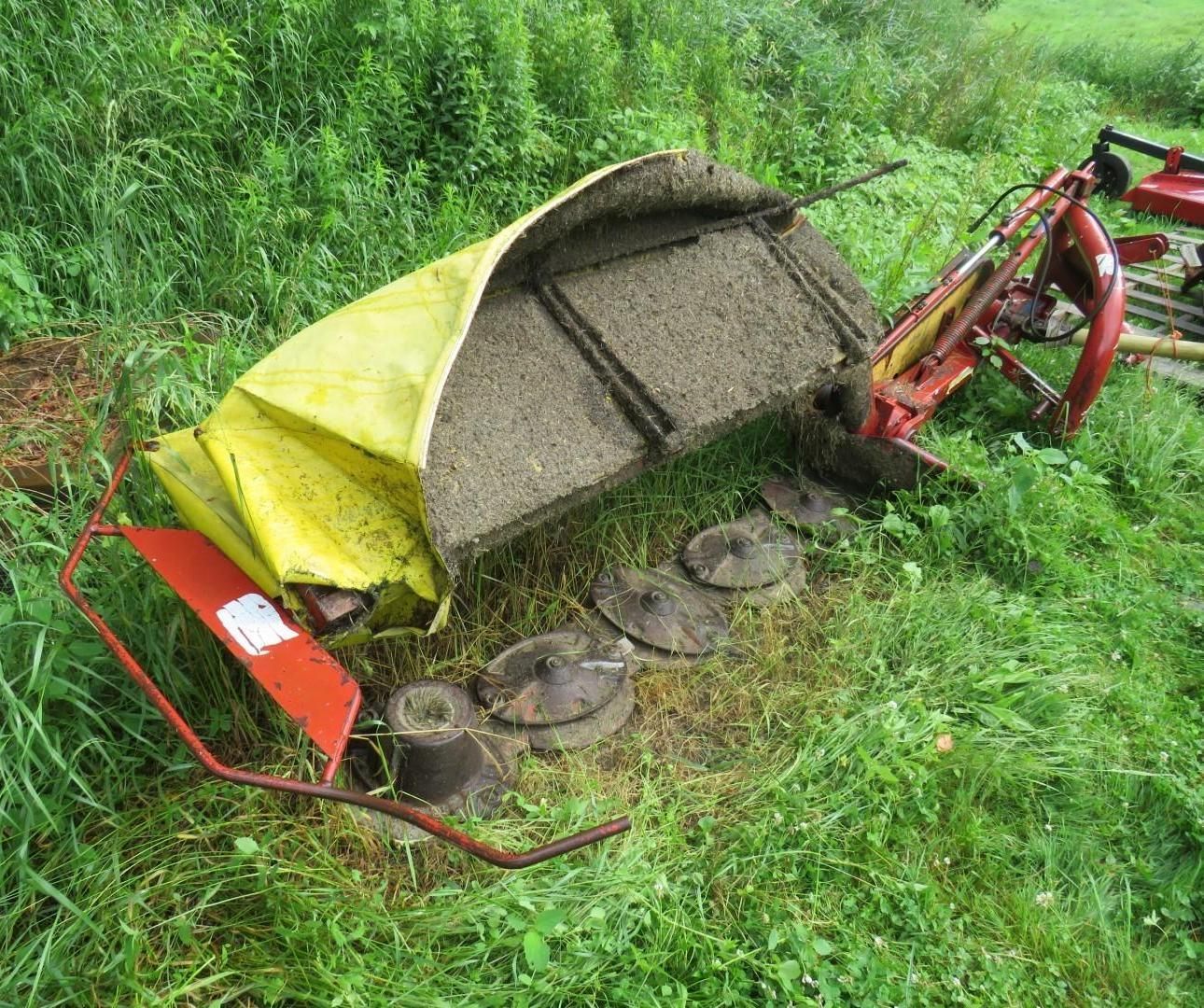 Rotary mower with yellow cover lying in a grassy field.