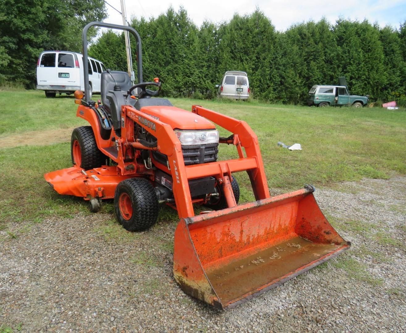 Orange Kubota tractor with a loader and mower in a grassy field.
