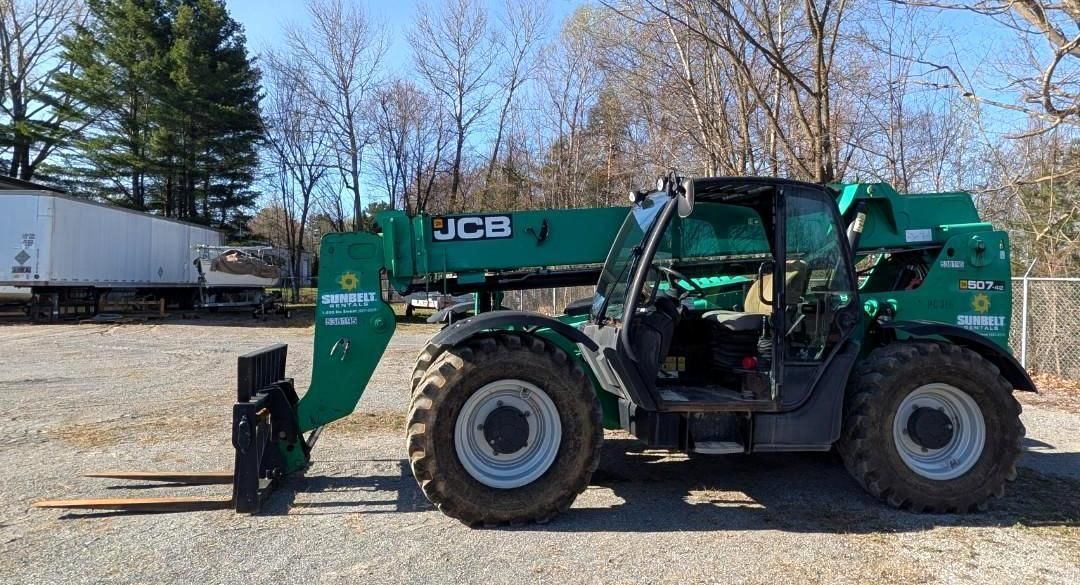 Green JCB telehandler parked outdoors on a gravel lot with trees and trucks in the background