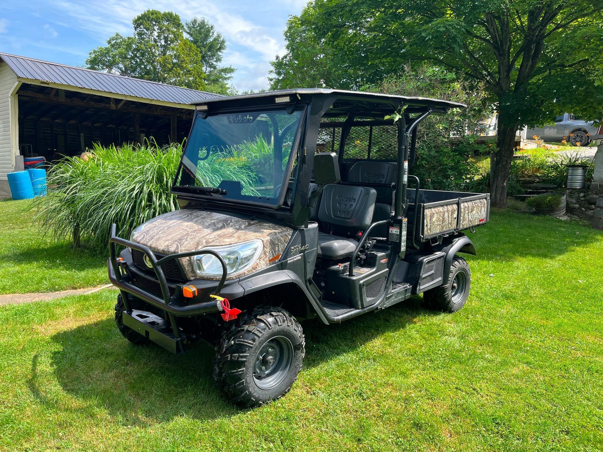 Camouflage utility vehicle on green grass; black frame, roof, and camo bed.