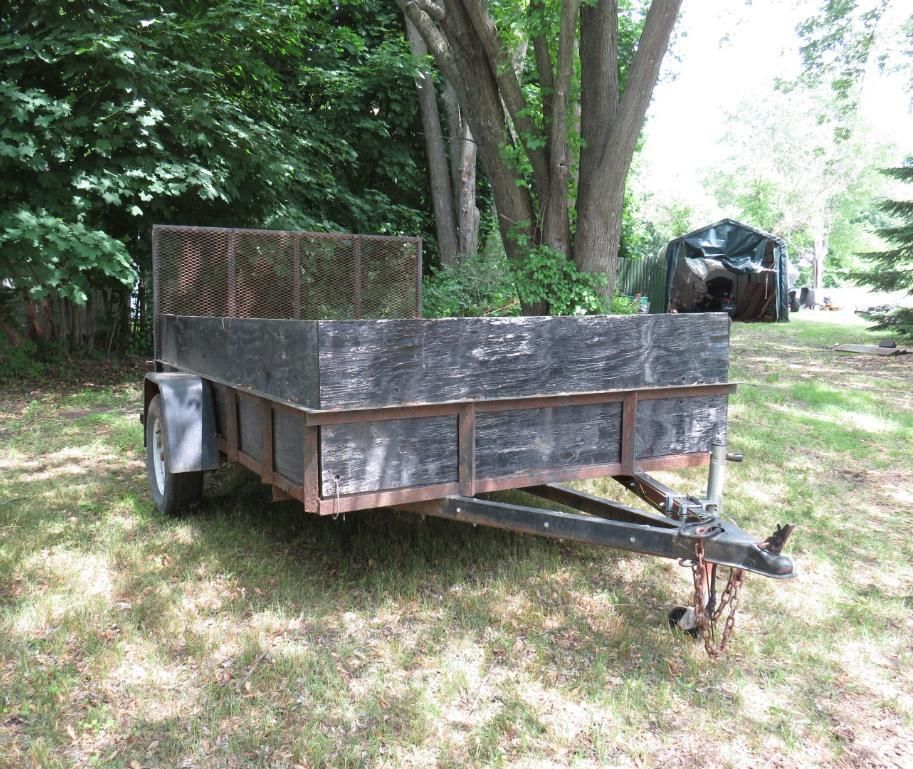 A utility trailer with wooden sides and a mesh back in a grassy yard.