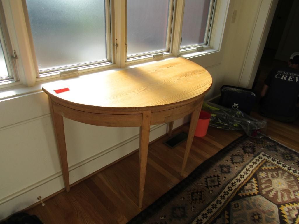 A light-wood, semi-circular table sits in front of a window. A patterned rug is on the floor.
