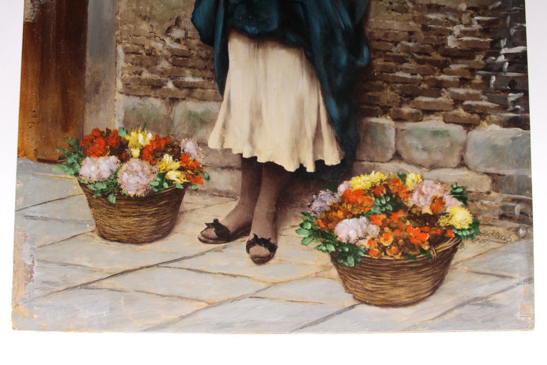 Woman in teal coat and cream skirt with two baskets of colorful flowers on a cobblestone street.