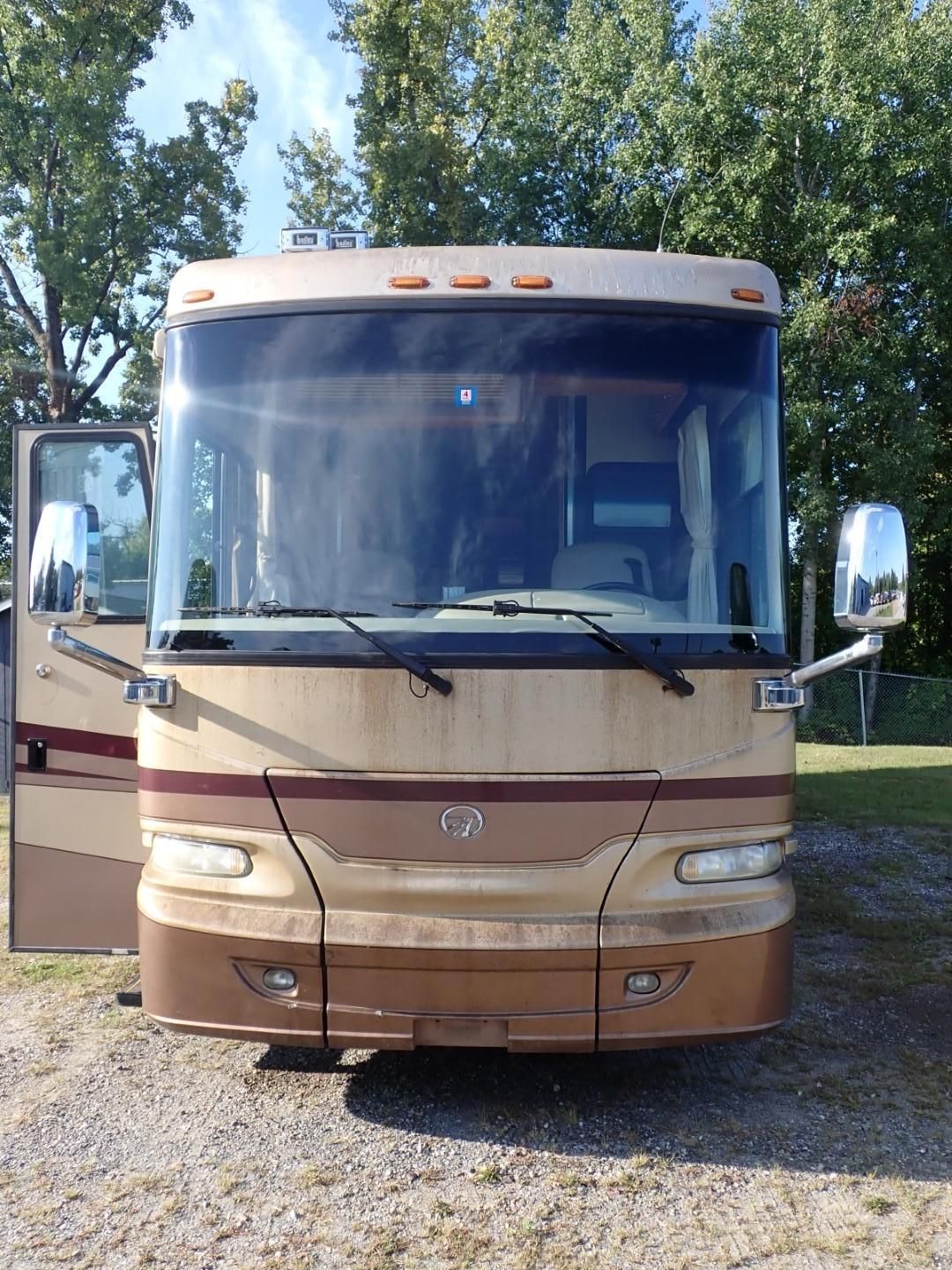 Tan and brown RV with the door open, parked on gravel.