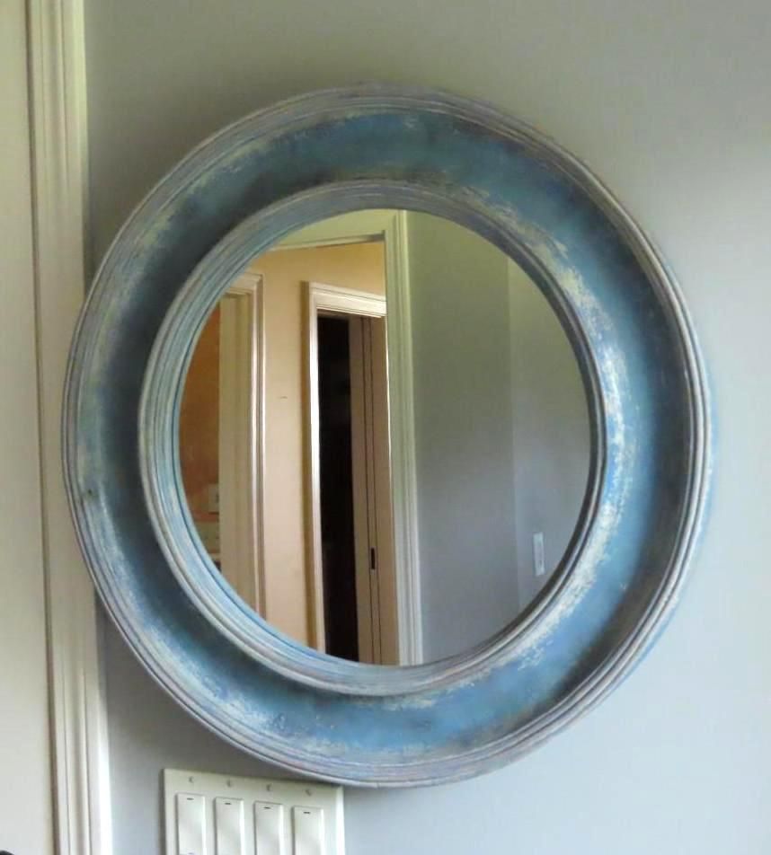 Round blue mirror with rough finish hanging on a gray wall.
