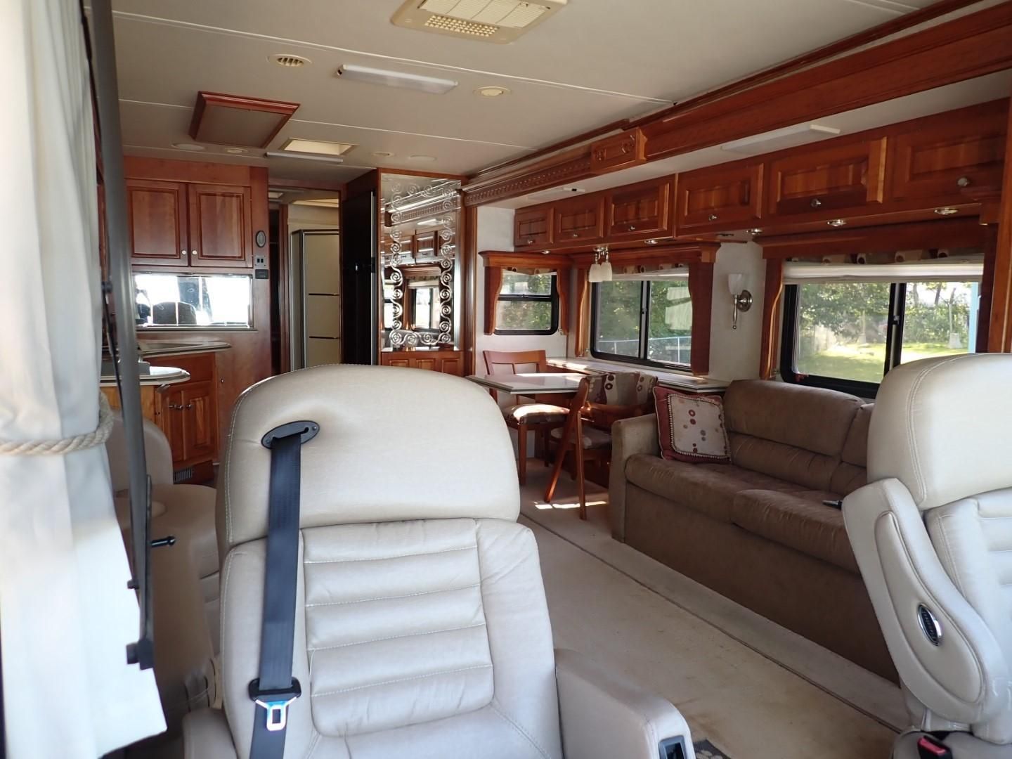 Interior of an RV with tan furniture, wood cabinets, and windows.