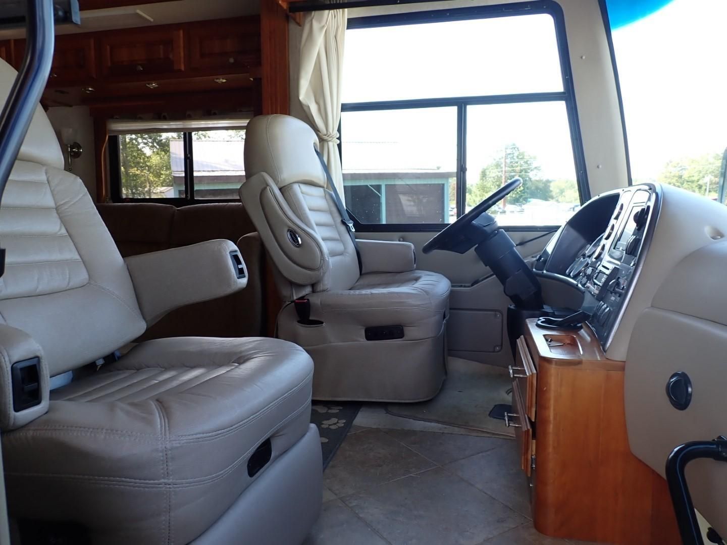 Interior of a motorhome with beige leather captain's chairs, steering wheel, and dashboard.