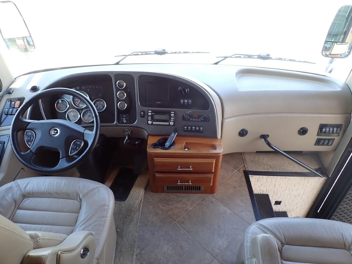 RV interior with driver's seat, dashboard with gauges, radio, wood accents, and tan seats.