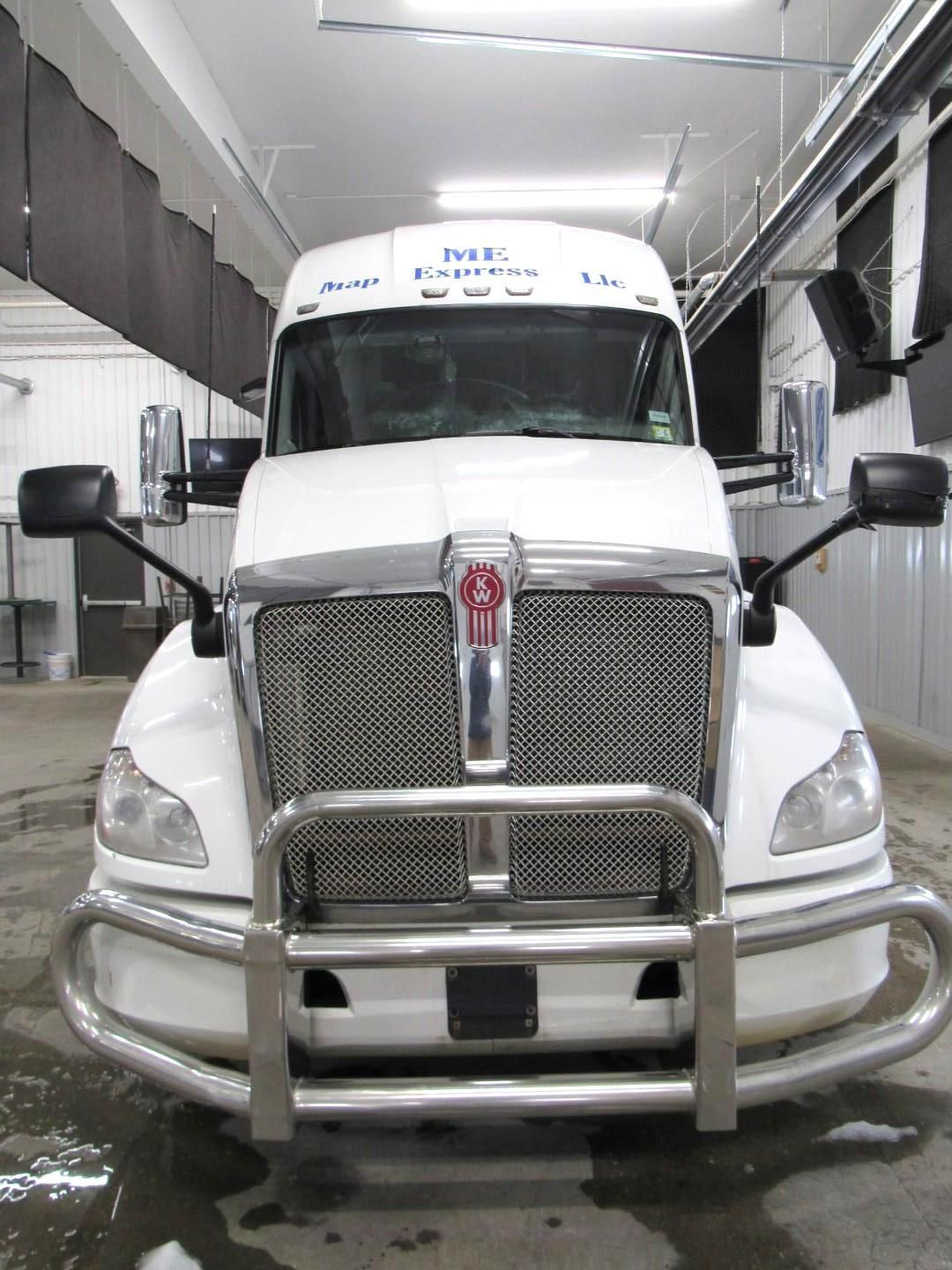 White semi-truck with chrome grill and bumper, parked indoors under bright lights.