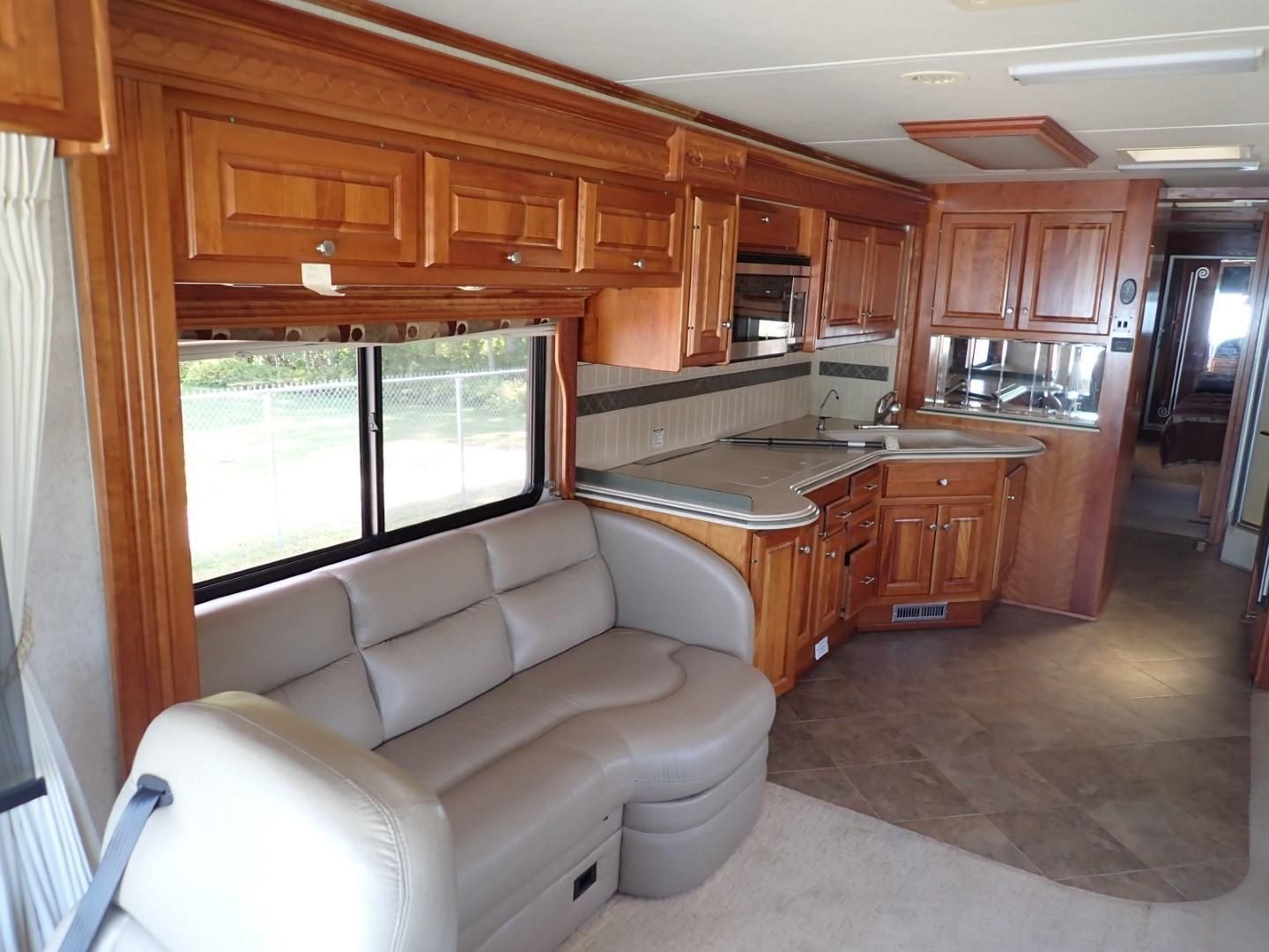 Interior of an RV with wooden cabinets, a gray sofa, a kitchen, and a window.