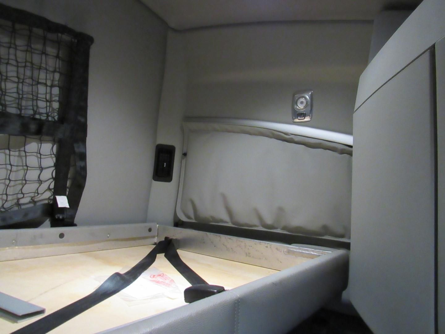 Interior of a semi-truck sleeper cab with bed, safety belts, and curtains. Gray and neutral tones.