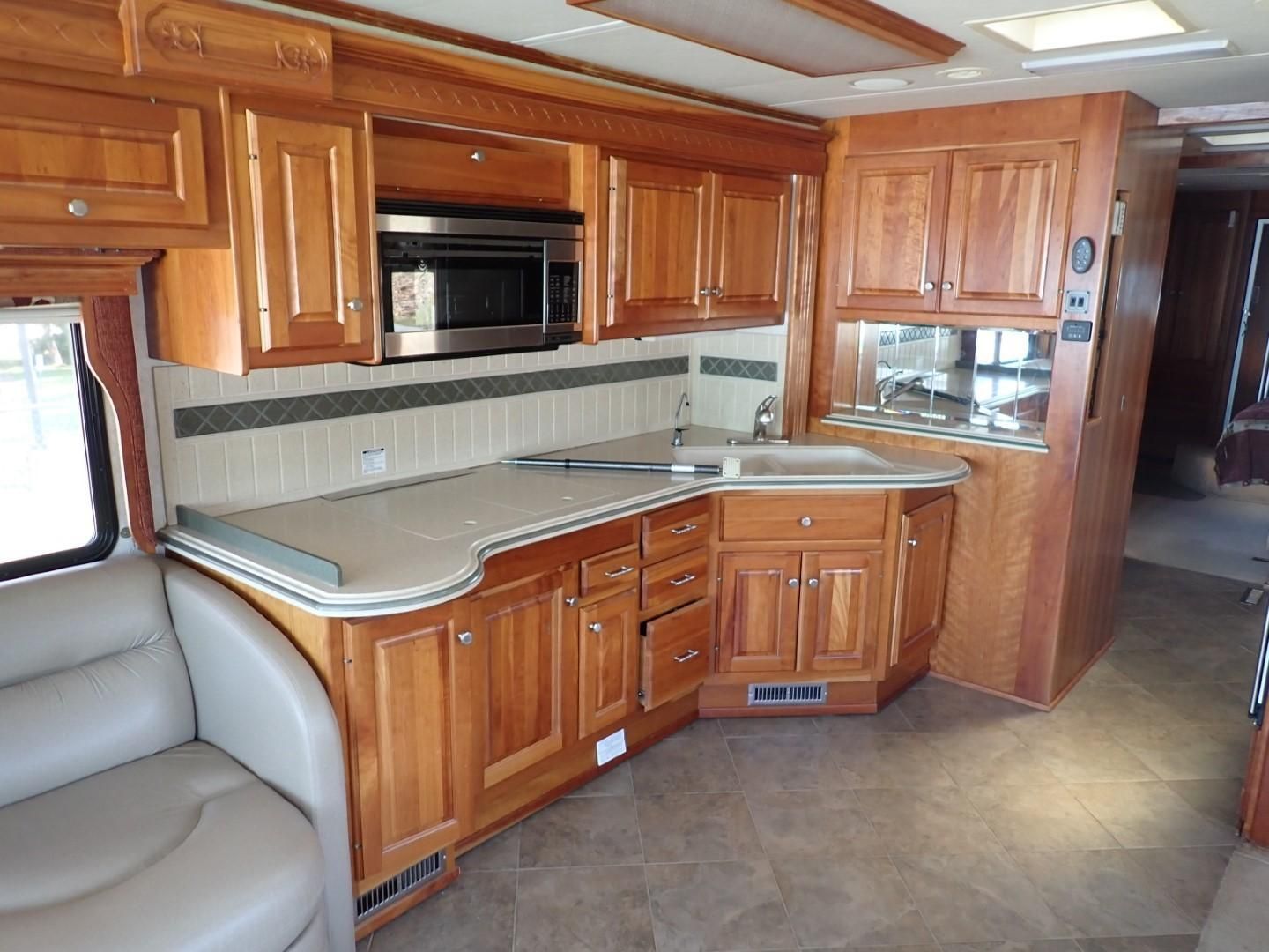 Interior of a motorhome kitchen with wooden cabinets, a sink, and a microwave.