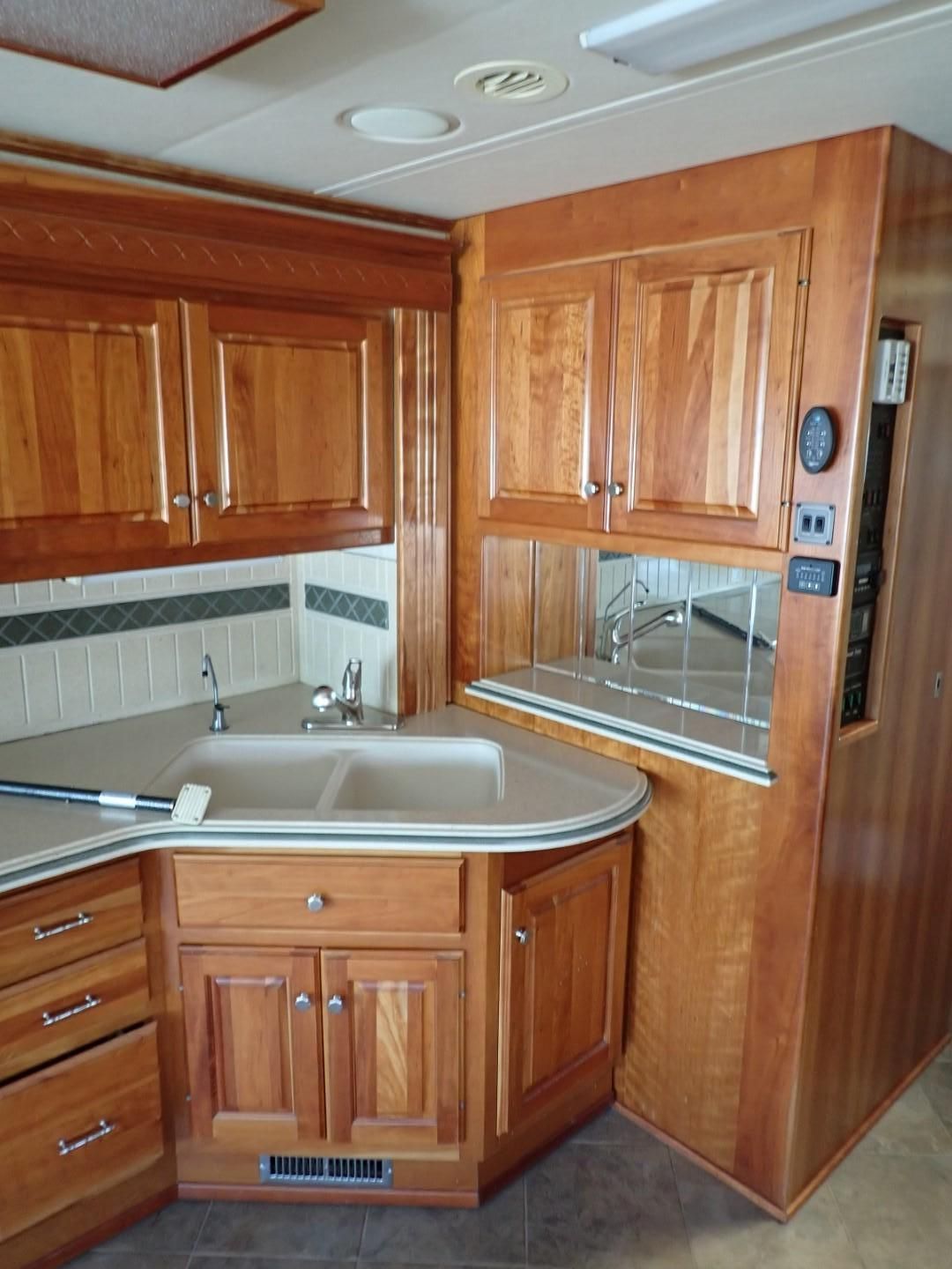 RV kitchen with light wood cabinets, sink, and tiled backsplash.