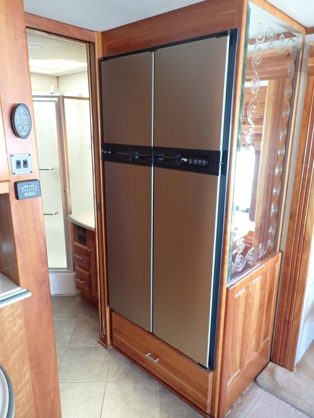 A refrigerator in a wooden cabinet, in a motor home. The bathroom is visible to the left.