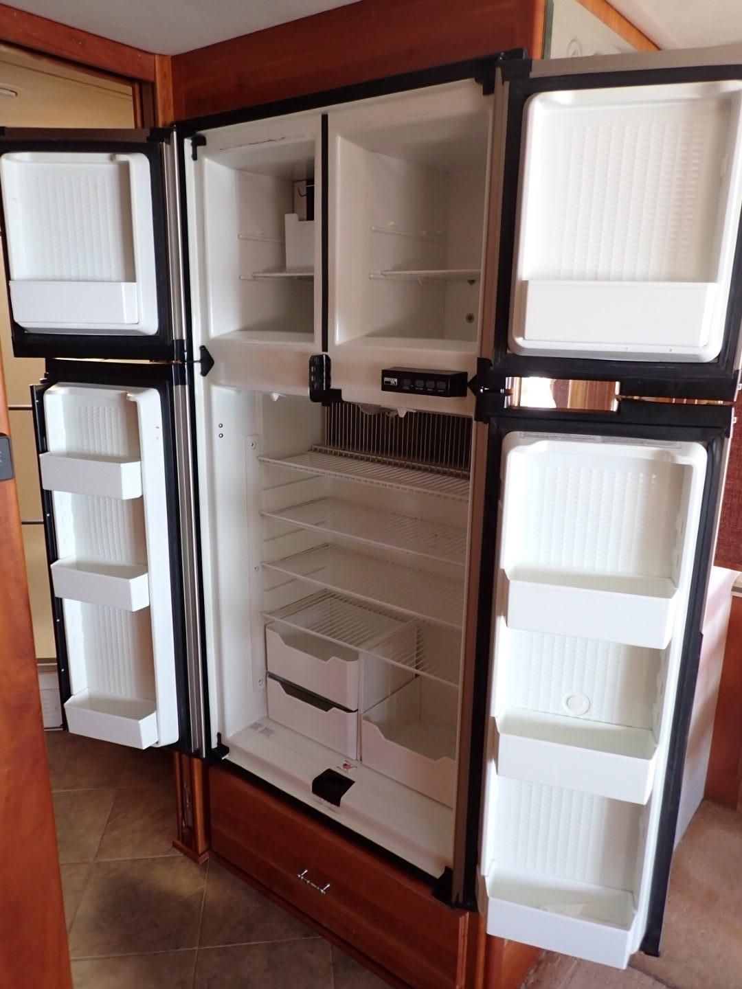 RV refrigerator with doors open, white interior, brown wood trim.