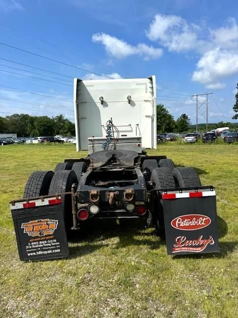 Rear view of a white Peterbilt truck cab with mud flaps on grass.