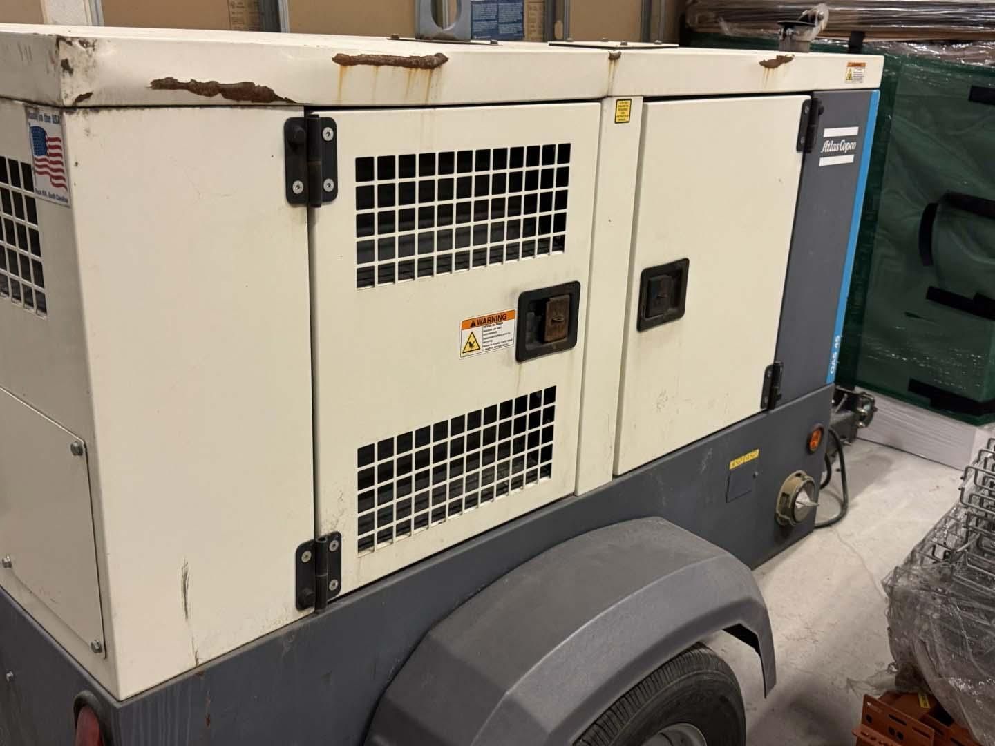 A cream and gray Atlas Copco generator on a trailer with metal vents.