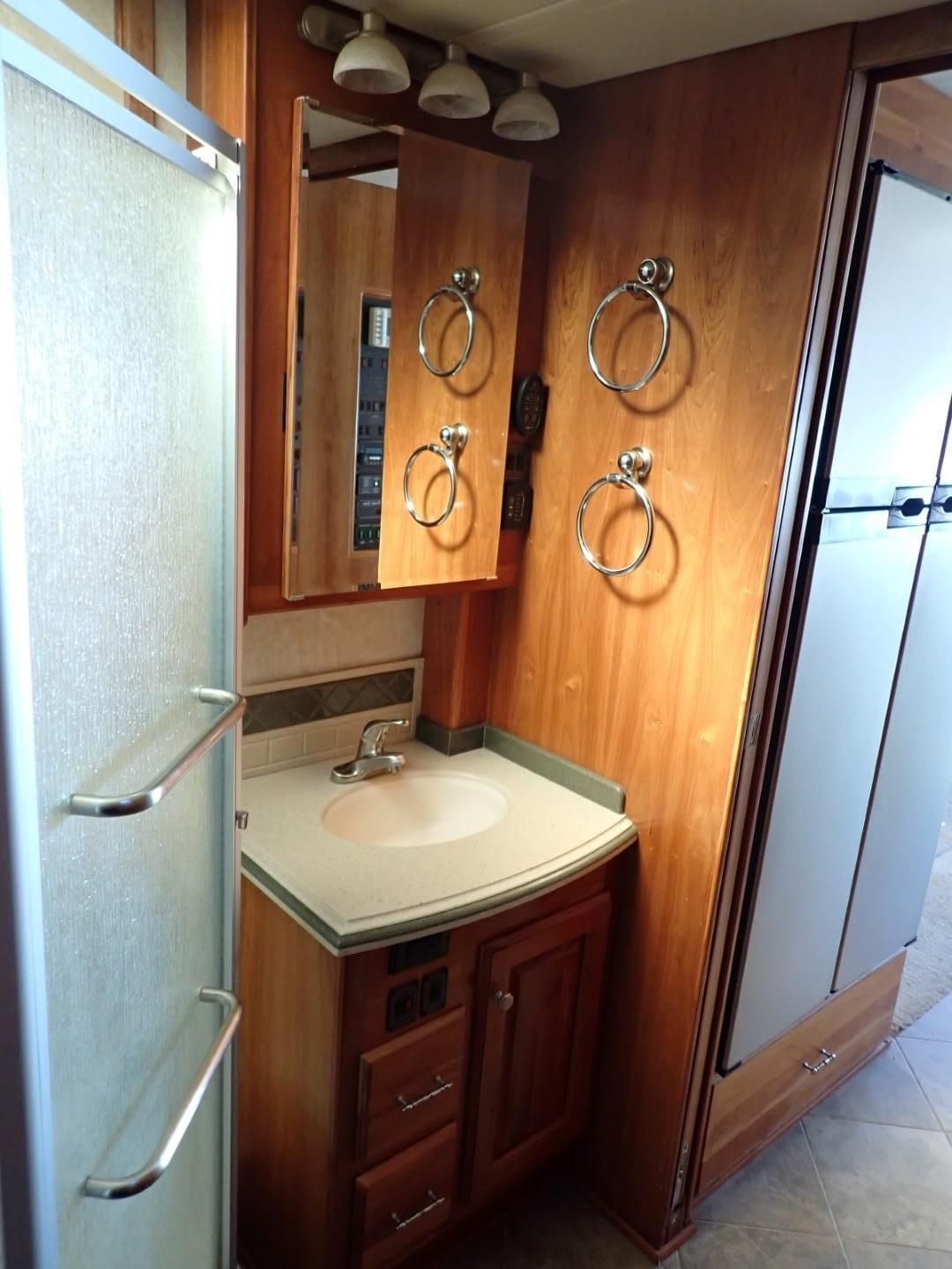 RV bathroom with a sink, mirror, towel rings, and shower. Wooden cabinets and walls.