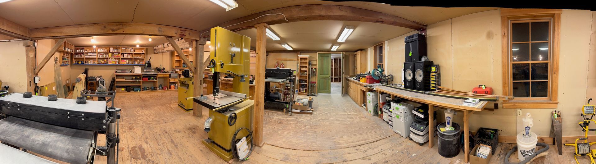 Panoramic view of a cozy workshop or studio with tables, shelves, tools, and warm lighting