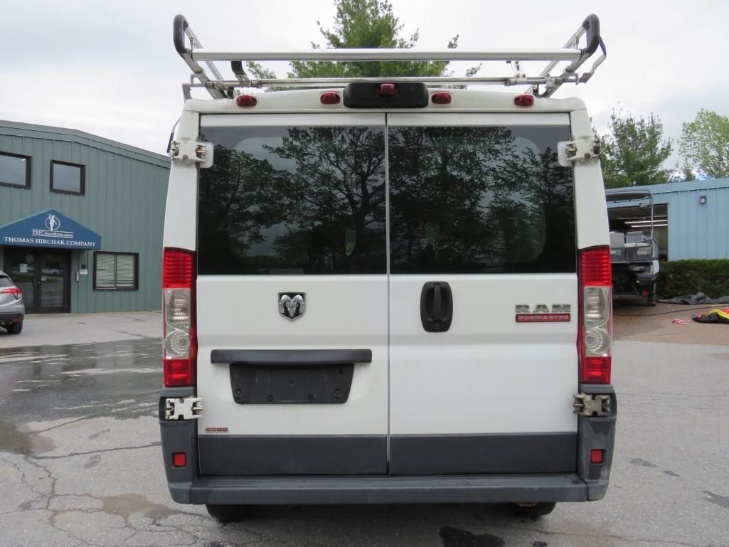 White RAM ProMaster cargo van, rear view, with roof rack, parked in front of a building.