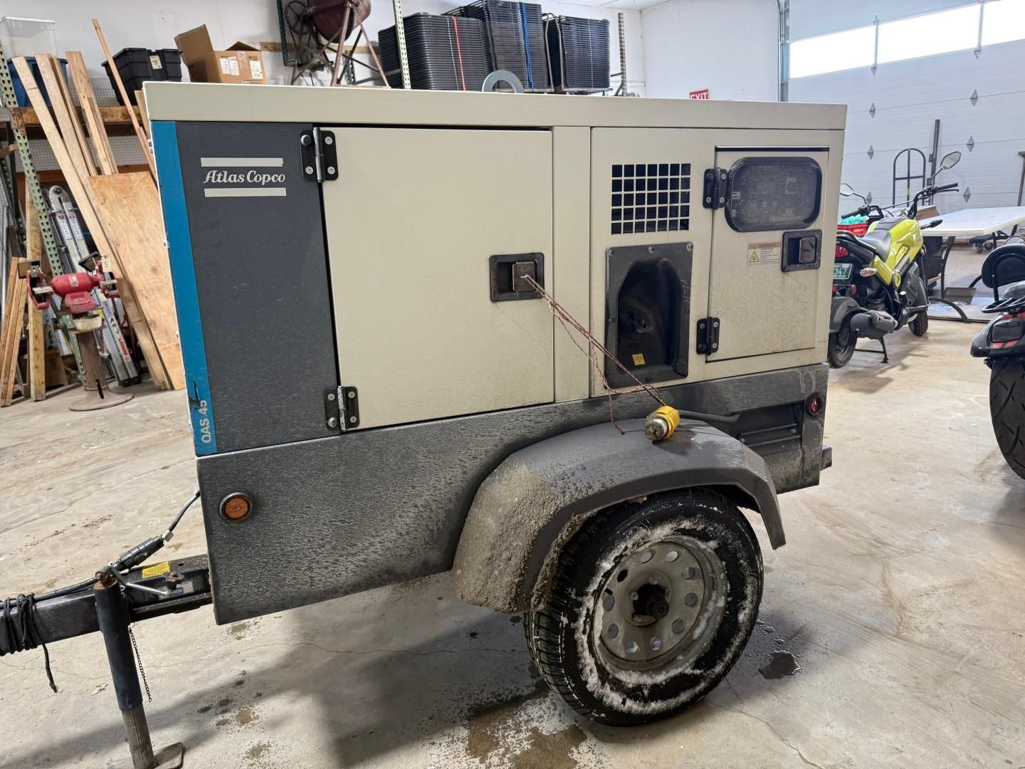 A beige Atlas Copco generator on a trailer, with blue and gray accents, parked in a garage.