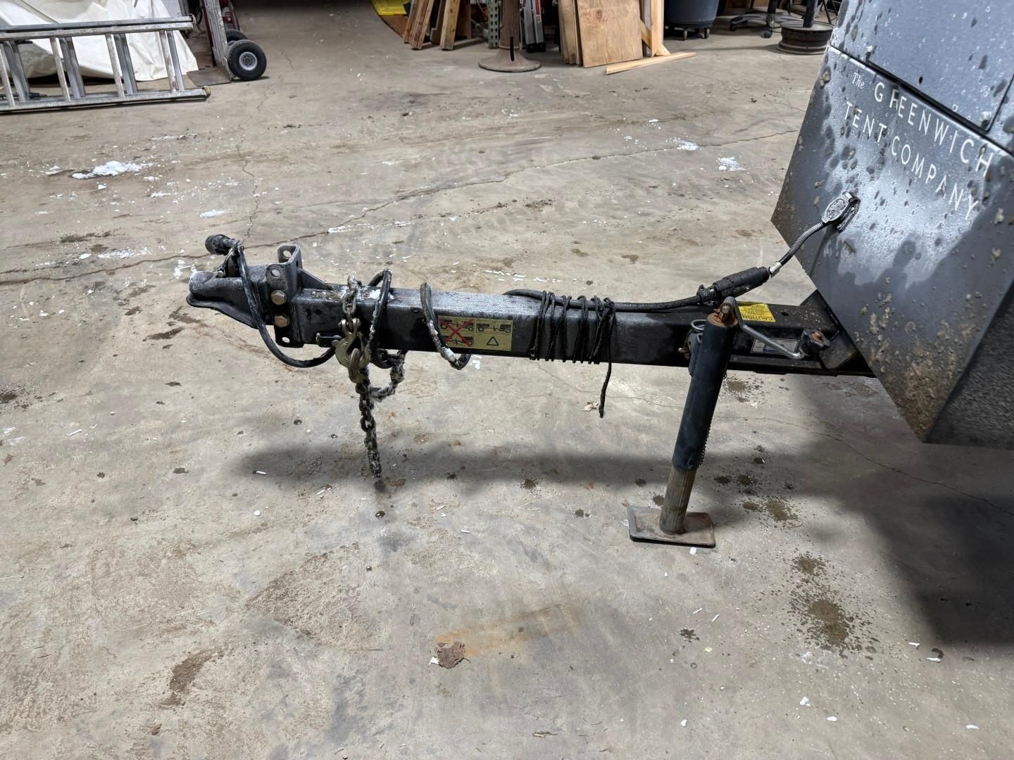 Trailer hitch on a trailer, with safety chains and jack on a concrete floor.