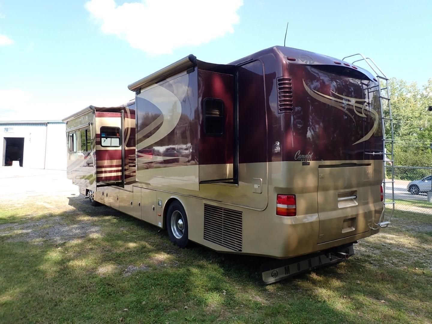 Burgundy and tan RV with open slide-out, parked on grass. Awning extended. Sunny day.