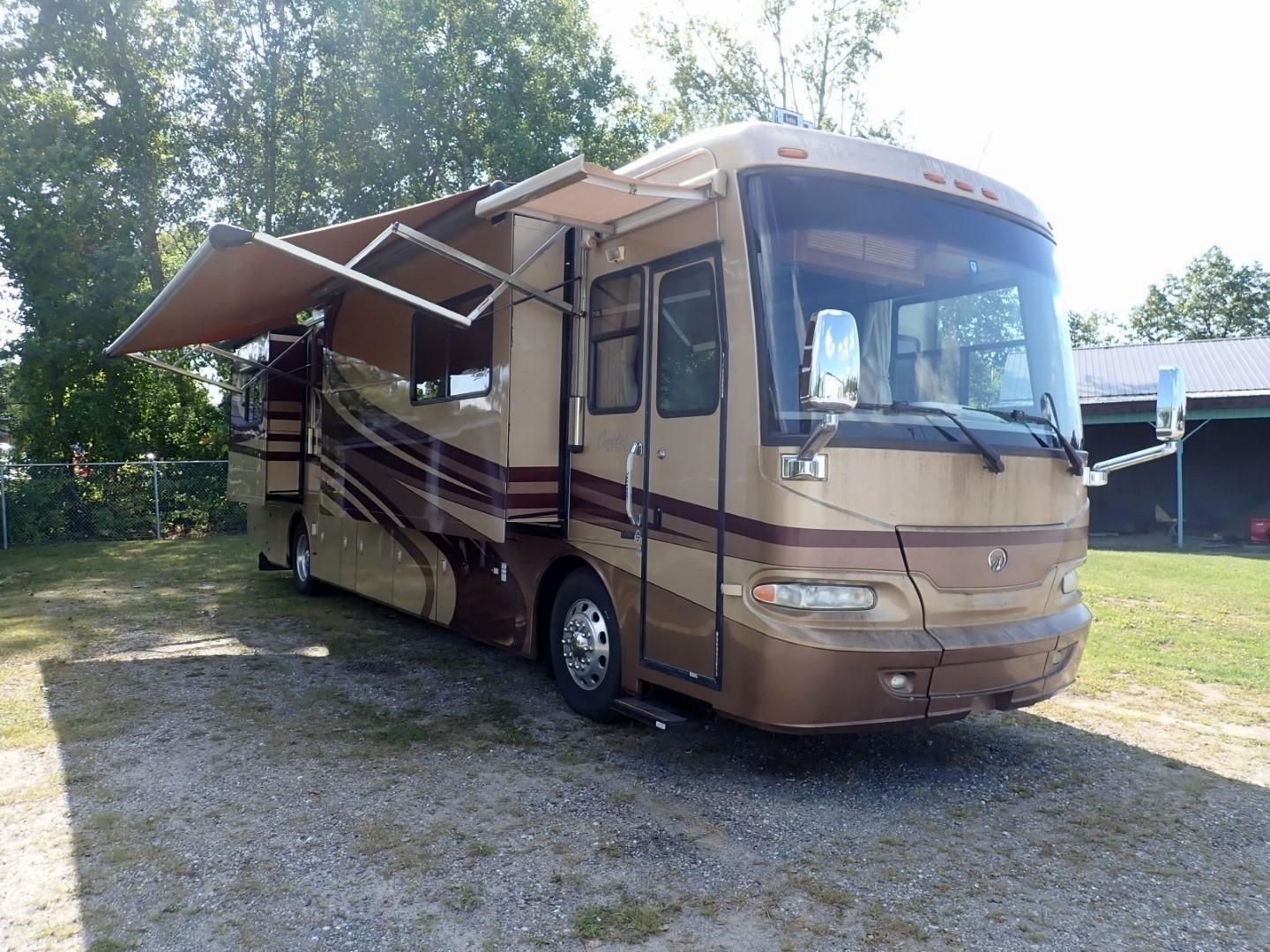 Tan and brown motorhome with awning extended, parked on gravel.