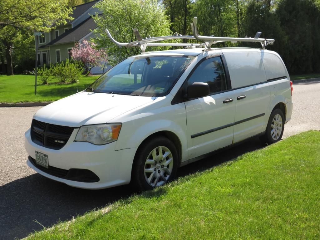 White cargo van parked on a paved road next to grass. Van has a roof rack.