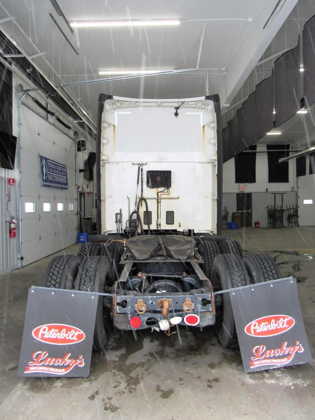 Rear view of a semi-truck in a garage, showcasing frame, tires, and Peterbilt mud flaps.