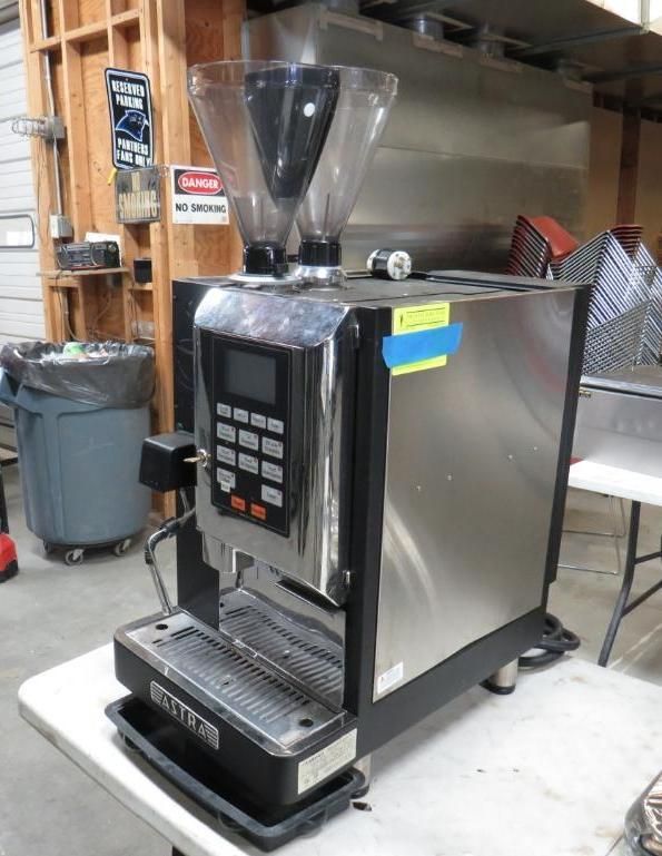 Espresso machine with grinder, stainless steel body, digital display, on a white table in a workshop.