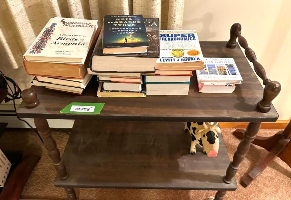 Wooden side table with books stacked on top and a toy cow on the lower shelf.