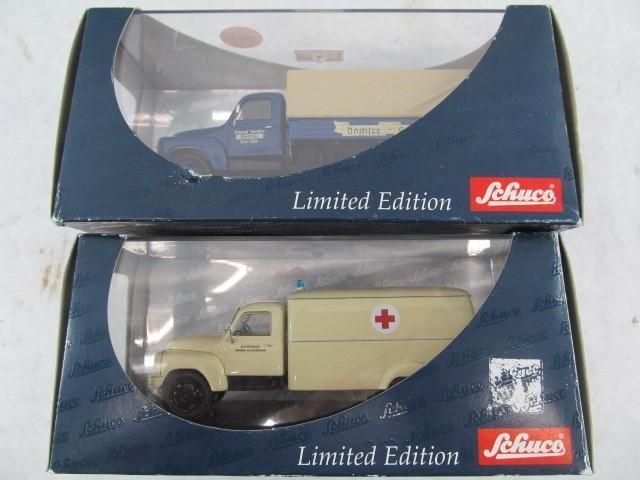 Two boxed Schuco Limited Edition diecast model trucks: a blue flatbed and a beige ambulance.