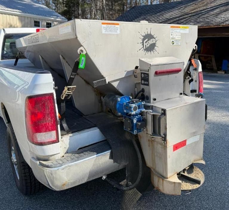 A white truck bed loaded with a stainless steel Fisher salt spreader for winter road maintenance.