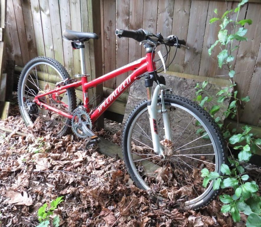 Red Specialized mountain bike propped against a wooden fence.
