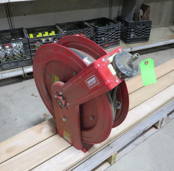 Red hose reel on wooden pallet, in front of shelves with crates and supplies.