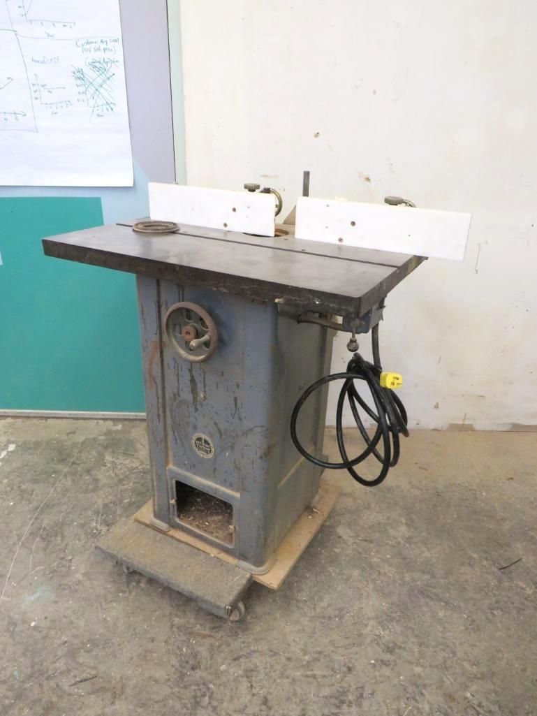A gray woodworking router table with a black tabletop and white fence, indoors.