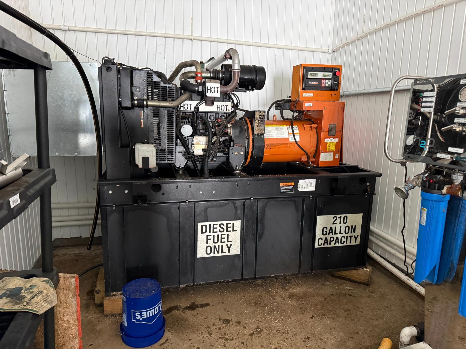 A diesel fuel generator inside a white walled room. It has an orange control panel and a sign stating 270 gallon capacity.