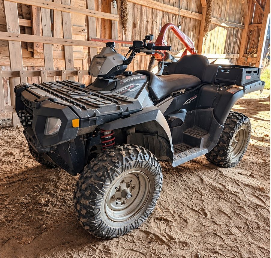 Black ATV parked inside a wooden barn with muddy tires and a cargo rack.