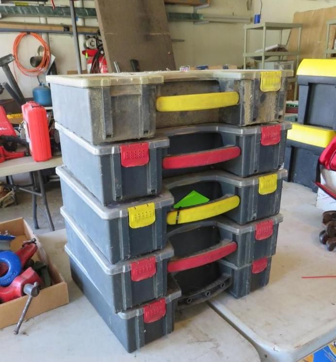 Stack of gray toolboxes with yellow and red handles, on a table in a garage.