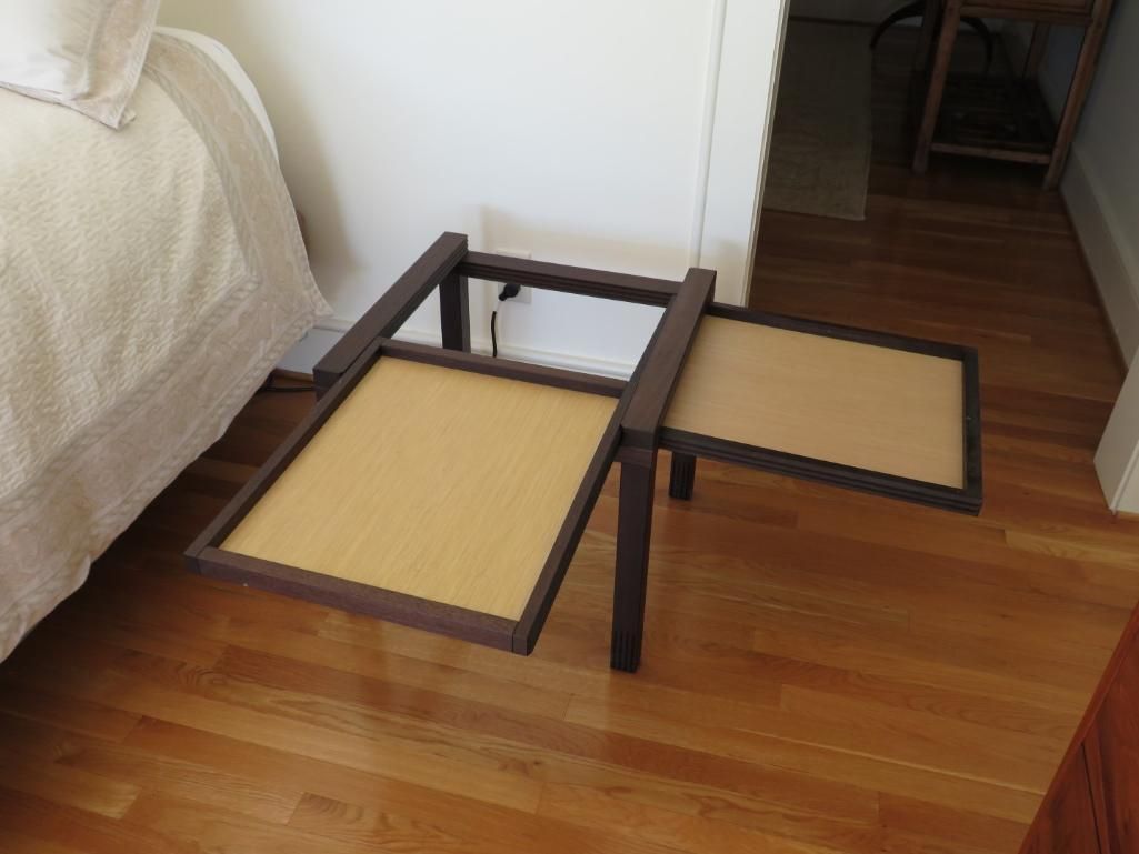 Brown folding table with two rectangular trays, on wood floor next to a bed.